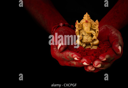 Hinduistische Elefantengott. Rotes Pulver bedeckt indischen mans Hand mit Lord Ganesha Statue vor schwarzem Hintergrund Stockfoto
