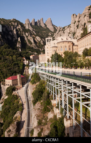 Eine vertikale Vorderansicht des Montserrat mit den Bergen im Hintergrund und vor. Auf der linken Seite ist die Schiene für Besucher Züge. Stockfoto