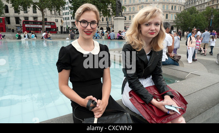 Zwei Mädchen im Teenageralter in Vintage-Kleidung, schwarzem Kragen und Handtaschen sitzen am Brunnen im Sommer Trafalgar Square London England Großbritannien KATHY DEWITT Stockfoto