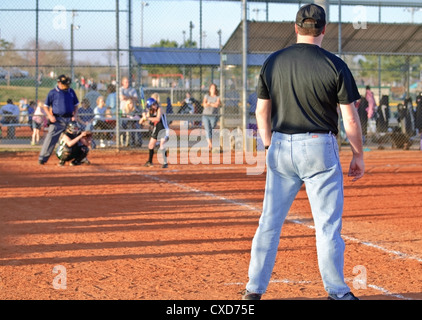 Aktion zu Hause Platte während eines Mädchens Softball-Spiel mit dem Trainer auf dem ersten Base. Stockfoto