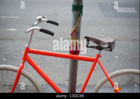 Orange Singlespeed Festrad Rennrad mit weißen Reifen, angekettet an einen Laternenpfahl Stadt mit gestrickten Graffiti. Stockfoto