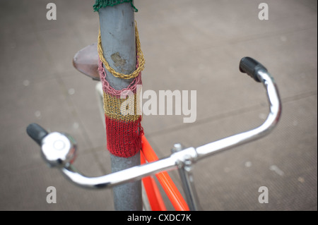 Orange Singlespeed Festrad Rennrad mit weißen Reifen, angekettet an einen Laternenpfahl Stadt mit gestrickten Graffiti. Stockfoto