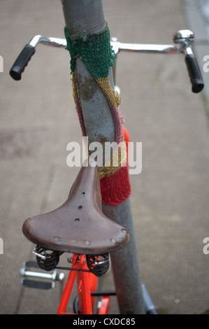 Orange Singlespeed Festrad Rennrad mit weißen Reifen, angekettet an einen Laternenpfahl Stadt mit gestrickten Graffiti. Stockfoto