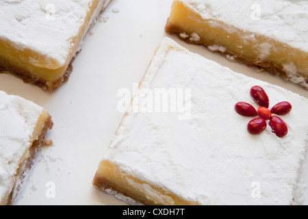 Abgewinkelt, Zitrone-Bars mit glatten Schicht von Konfekt Zucker mit Candy Rot Blume als Akzent auf weißen Teller. Stockfoto