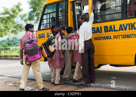 Indian School Kinder erhalten auf einen Schulbus betreut von einem Lehrer. Puttaparthi, Andhra Pradesh, Indien Stockfoto