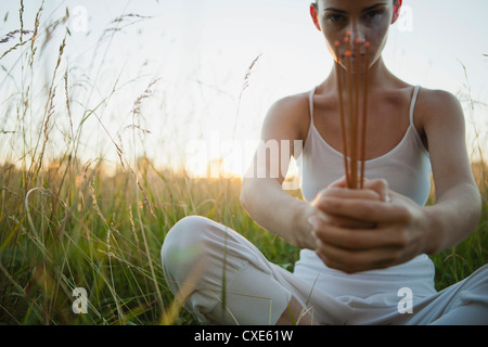 Junge Frau sitzt im Rasen, hält Räucherstäbchen Stockfoto