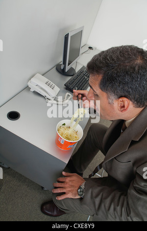Kaufmann Essen Ramen-Nudeln am Schreibtisch im Büro Stockfoto
