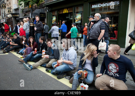 Junge Leute Essen McDonalds Fastfood auf der Straße in London. Stockfoto