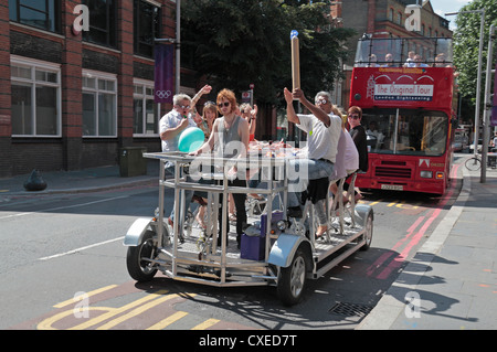 Touristen, Radfahren auf ein Pedibus, ein Party-Bike-Erlebnis in London, Vereinigtes Königreich.  Hinter gekrönt in einem eher traditionellen offenen Bus-Tour. Stockfoto