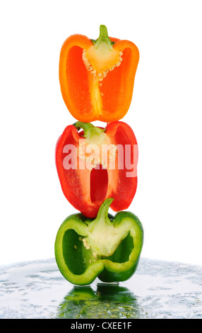 Ein Stapel von drei Paprika, die in zwei Hälften geschnitten worden sind. Hochformat in weiß mit Reflexion in der nassen Tischplatte. Stockfoto