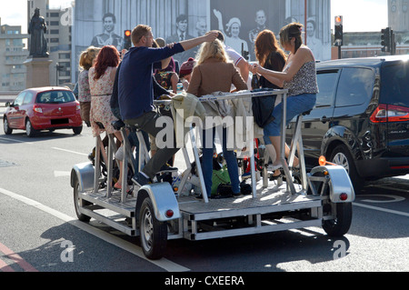 Eine Gruppe von Männern und Frauen genießen eine energiegeladene Tour durch London mit dem Pedi-Bus, auch bekannt als Party-Bike, Bier, Fahrradpedal, Crawler, Pedal, Pub, Party-Bike, England, Großbritannien Stockfoto