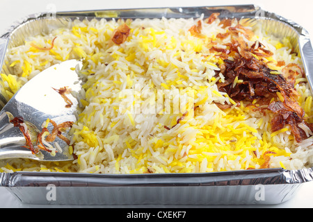 Ein indisches Restaurant Pilau Reis mit Zwiebeln garniert mitnehmen in eine Aluminium-Schale mit einem Löffel Reis servieren Stockfoto