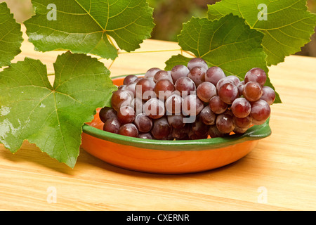 Rote Trauben und Blätter auf Holztisch Stockfoto