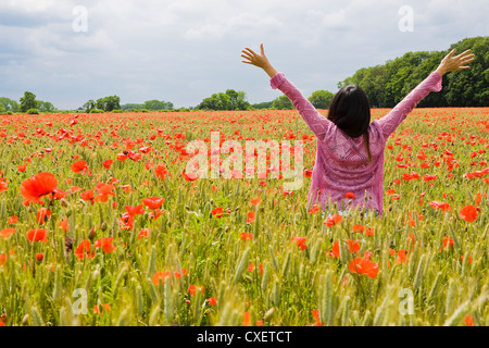 Dunkelhaarige Frau hält ihre Arme in einem englischen Weizenfeld umgeben von Mohn Stockfoto