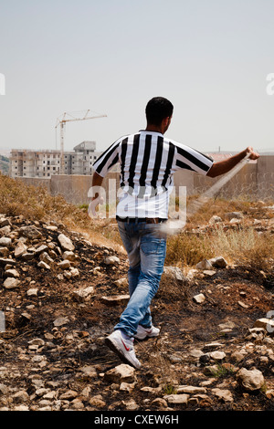 Nach der Bombardierung von Tränengas rächt sich palästinensische Demonstranten mit Steinen auf israelische Sicherheitsmauer im Dorf Bi'lin Stockfoto