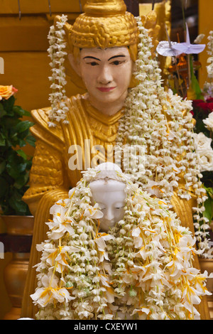 Eine BUDDHA-STATUE, bedeckt mit Blumen an der SHWEDAGON PAYA oder Pagode aus dem Jahre 1485 - YANGON, MYANMAR Stockfoto