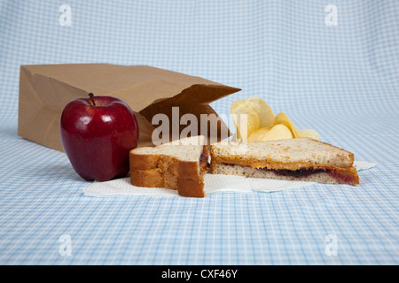 Lunchpaket mit Erdnussbutter, Apfel und Chips auf eine blau karierte Tischdecke Stockfoto