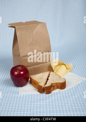 Lunchpaket mit Apfel, Sandwich und Chips auf eine blau karierte Tischdecke Stockfoto