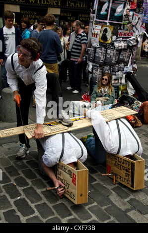 Männer mit ihren Köpfen in Holzkisten und ein weiteres sägen Holz, eine Show in dem Edinburgh Festival Fringe, Schottland zu fördern. Stockfoto