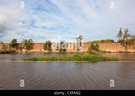 Ein ummauerter Garten eingetaucht unter Hochwasser im Herbst mit Bäumen und roten Traktor bei bewölktem Himmel blau Stockfoto