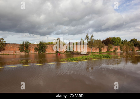 Ein ummauerter Garten eingetaucht unter Hochwasser im Herbst mit Bäumen und unter Wasser roten Mini-Traktor bei bewölktem Himmel blau Stockfoto