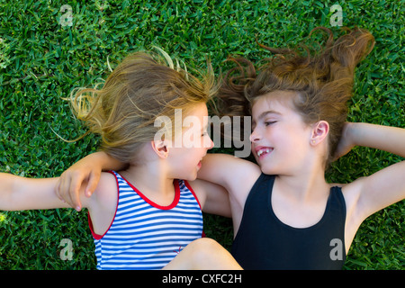 Blond und brünett Schwestern Kind Mädchen lächelnd auf Gartengras liegend Stockfoto