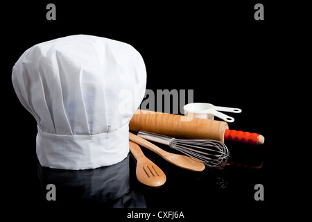 Eine Kochmütze mit Kochutensilien auf einem schwarzen Hintergrund mit Textfreiraum Stockfoto