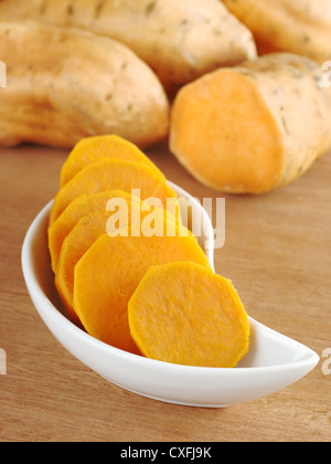 Süßkartoffel (Ipomoea Batatas lat.) schneiden Sie in Scheiben in weiße Schüssel auf Holzoberfläche mit Süßkartoffeln im Hintergrund gekocht Stockfoto