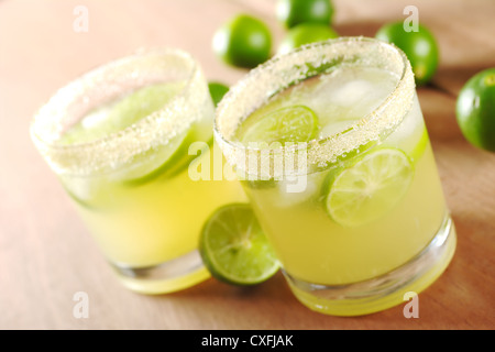 Frische Limonade mit Limettenscheiben und Eiswürfel in einem umrandeten Zucker Glas umgeben von Limes auf Holz Stockfoto
