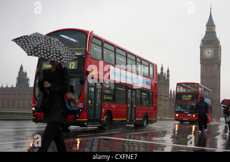 Menschen zu Fuß über Westminster Brücke im Regen mit Big Ben im Hintergrund und zwei Doppeldecker-Busse vorbei Stockfoto