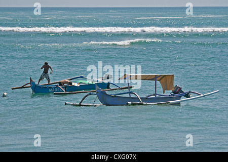 Zwei Männer in einem Jukung am Strand von Kuta, Bali, Indonesien. Jukung sind traditionelle indonesische Boote. Stockfoto