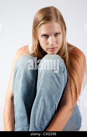 Schöne blonde Frau sitzt mit ihrem Knie in der Nähe von ihr Kinn, hob mit einem nachdenklichen Blick in die Kamera schaut Stockfoto