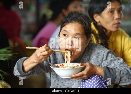 Vietnam, Marktfrau, eine asiatische Nudelpfanne mit Stäbchen zu essen Stockfoto