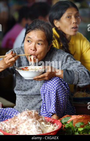 Vietnam, Marktfrau, eine asiatische Nudelpfanne mit Stäbchen zu essen Stockfoto