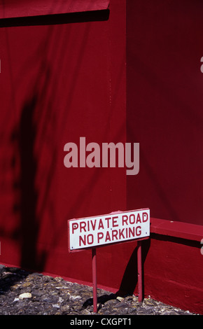Detail der Mauer und Gebäude mit Telefonmast Schatten und Zeichen auf Laufwerk Private Road No Parking rot lackiert Stockfoto