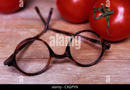 Vintage Schildpatt Brille mit runden Gläsern liegen auf hölzernen Tisch oder Regal neben reife Tomaten Stockfoto