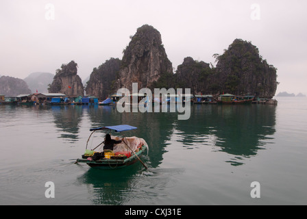 Handel mit Boot nähert sich einem schwimmenden Dorf und Kalkstein Karst Felsformationen, Halong Bucht, Vietnam Stockfoto
