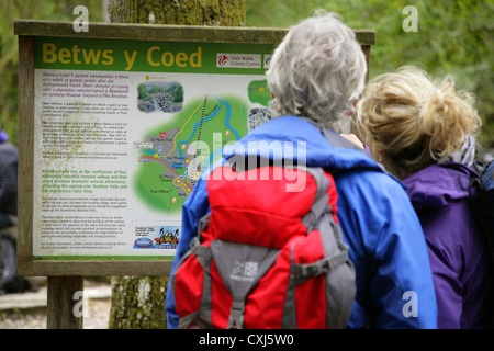 Touristen auf der Suche bei der Touristeninformation Sign. in Betws-y-Coed, Conwy, Nordwales Stockfoto