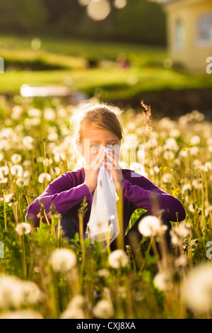 Mädchen sitzen auf einer Wiese mit Löwenzahn und hat Heuschnupfen oder Allergie Stockfoto