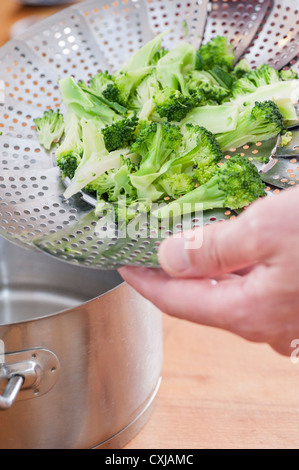 Nahaufnahme des Menschen kochen Brokkoli, bereitet das Gemüse in einen Topf mit einem Dampfer utensil Stockfoto