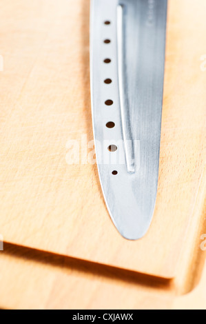 Messer mit Löchern auf Holzbrett liegend Stockfoto