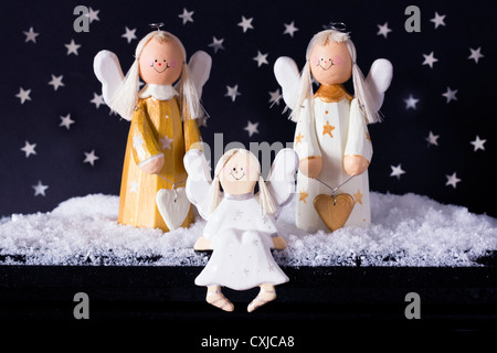 Drei goldenen und weißen dekorativen hölzernen Engel im Schnee vor einem Sternenhimmel schwarzen Hintergrund. Stockfoto
