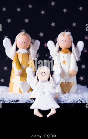Drei goldenen und weißen dekorativen hölzernen Engel im Schnee vor einem Sternenhimmel schwarzen Hintergrund. Stockfoto