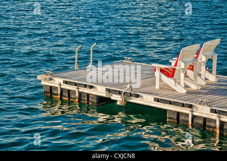 Zwei Adirondack Stühle auf ein Schwimmdock bei Sonnenuntergang. Stockfoto