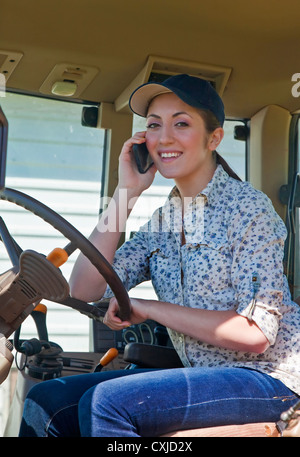 Junge Bäuerin spricht über ihr Telefon in der Kabine von ihrem Traktor. Stockfoto