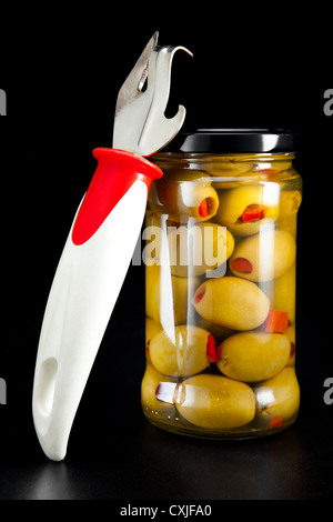Glas mit verzinnten Oliven und ein Dosenöffner Stockfoto