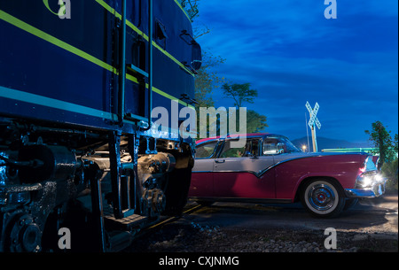 Blaue Zug Eisenbahn Dieselmotor trifft fast Oldtimer Thunderbird Auto am Bahnübergang in der Nacht Stockfoto
