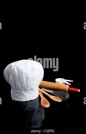 Kochmütze und verschiedene Utensilien auf einem schwarzen Hintergrund mit Textfreiraum Stockfoto