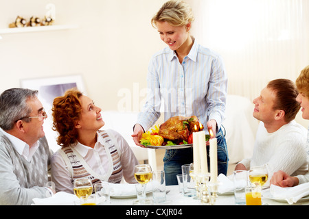 Porträt der Großfamilie am festlich gedeckten Tisch sitzen und Blick auf hübsche Frau mit Schale gebratenen Truthahn Stockfoto
