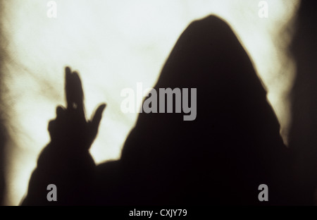 Schatten der vermummten Mönch oder Priester hielt seine Hand und Finger in Segen vor dem hellen Fensterlicht Stockfoto